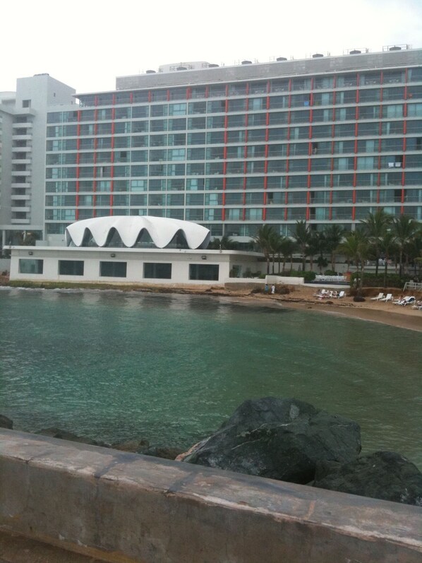 A hotel with a modern design, featuring a large building with a distinctive white dome structure and a multi-story facade with red accents. - San Juan Condo on the beach (San Juan)