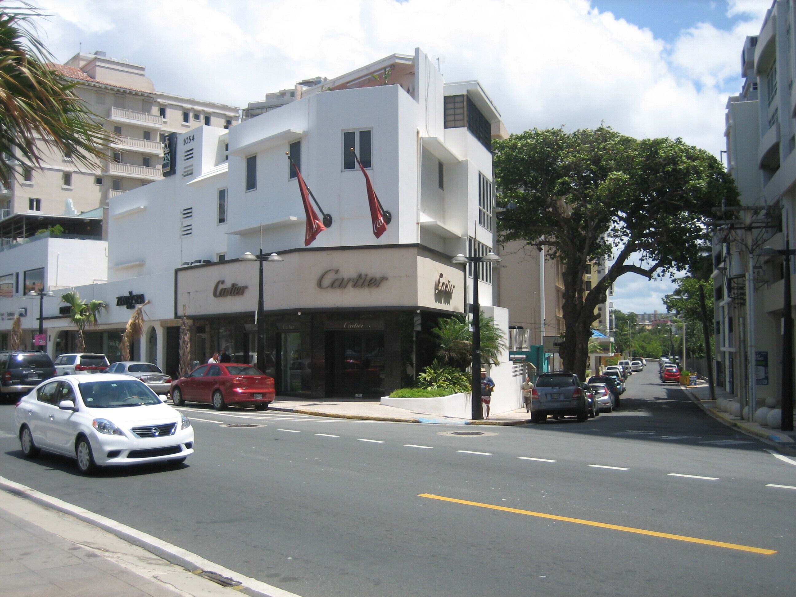 Une vue de rue avec un bâtiment portant l’inscription « Cartier » et plusieurs voitures garées le long de la route.
