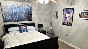 A bedroom with a bed, a nightstand, a lamp, a chair, and a wall with artwork and a sign. - SUPER SUMMER SAVINGS!! ;:HOT PROPERTY (baton rouge)
