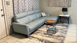 A living room with a light blue sofa, a patterned curtain, a wooden coffee table, a small side table with a lamp, and a rug. - SUPER SUMMER SAVINGS!! ;:HOT PROPERTY (baton rouge)