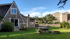 Ein Wohnhaus mit geneigtem Dach, einer Veranda und einem Hinterhof mit Picknicktisch und Feuerstelle.