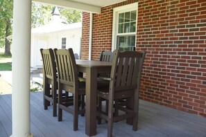 A wooden dining table with four chairs on a covered porch with a brick wall.