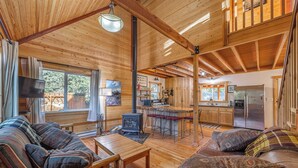 A wooden cabin interior with a sofa, dining table, kitchen area, and a fireplace.