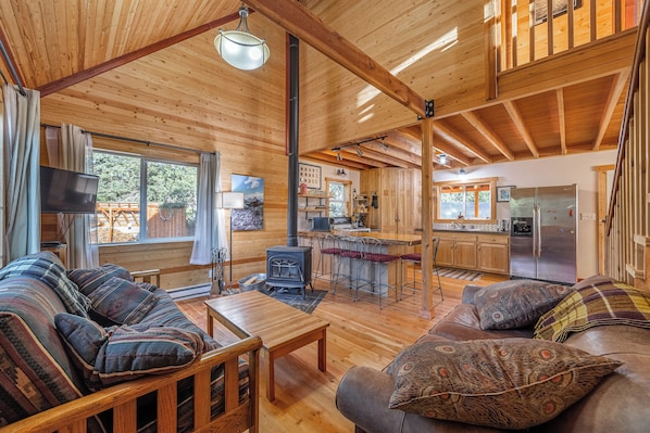 A wooden cabin interior with a sofa, dining table, kitchen area, and a fireplace.