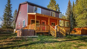 A two-story wooden cabin with a wooden deck and stairs leading to a covered porch.