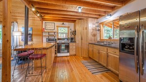 A wooden cabin kitchen with a large stove, refrigerator, and wooden cabinets.