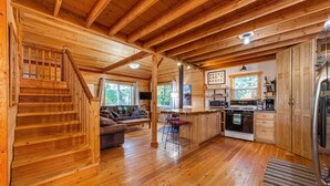 A wooden cabin interior with a kitchen, dining area, and a staircase.