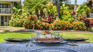 A dining setup with a dessert on a plate, surrounded by cutlery and glasses, set on a patterned tablecloth. - Spacious Studio Beach Chic, Walk to Sandy Napili Bay-Napili Shores C116 (Lahaina)