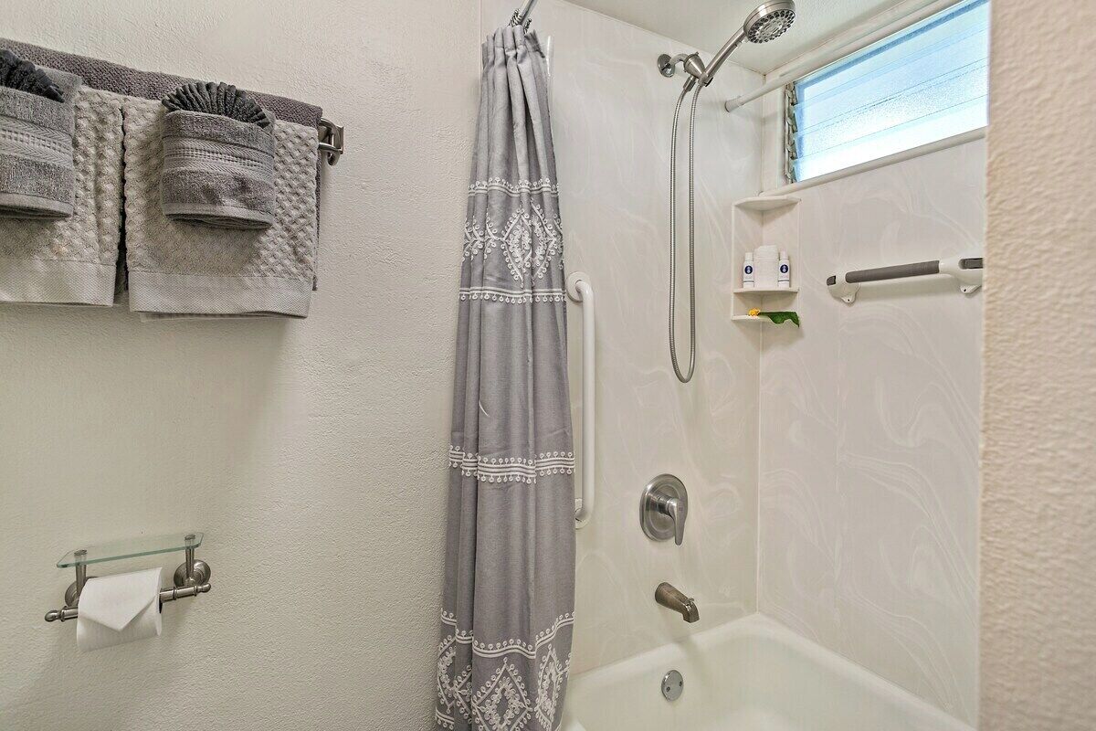A bathroom with a shower, a glass shelf with toiletries, and towels hanging on the wall.