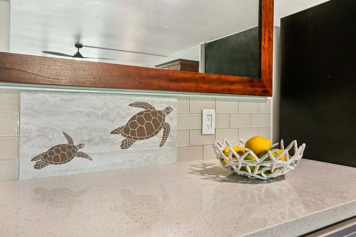 Une cuisine avec un plan de travail, un panier blanc rempli de citrons et un pare-feu décoré de motifs représentant des tortues de mer.