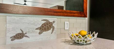 Une cuisine avec un plan de travail, un panier blanc rempli de citrons et un pare-feu décoré de motifs représentant des tortues de mer.