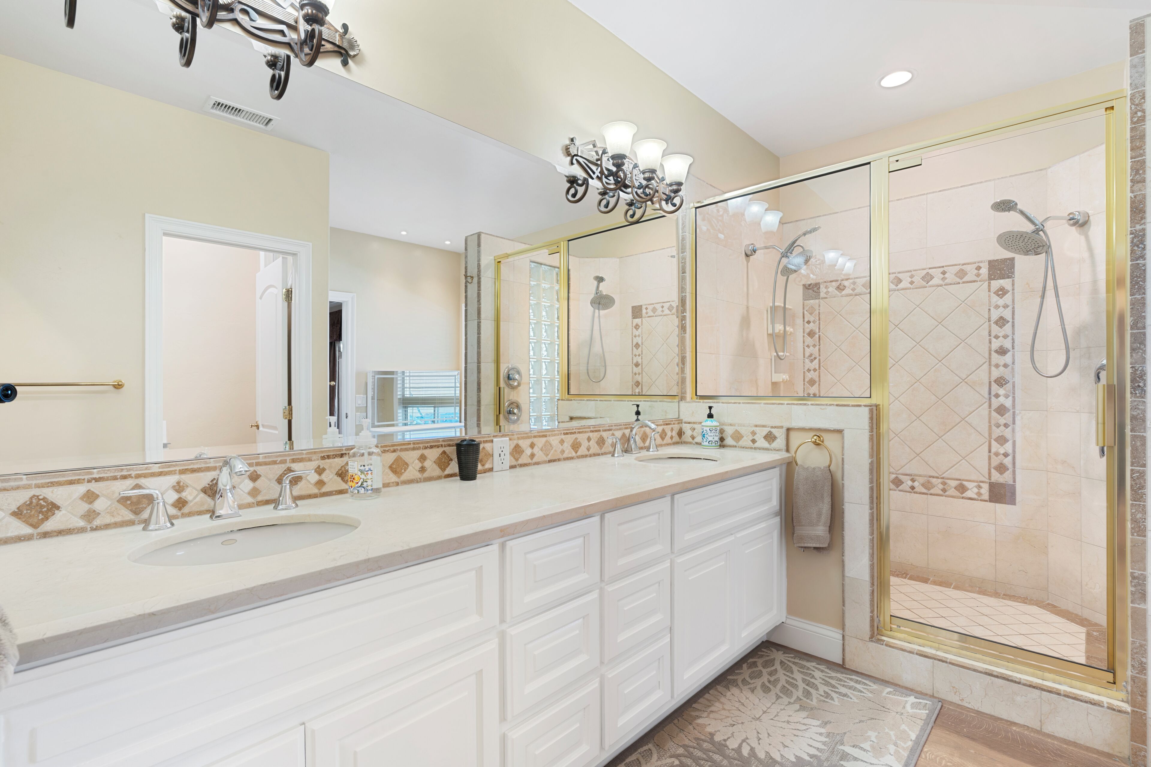 A bathroom with a large vanity, two sinks, a shower with a glass door, and a chandelier.