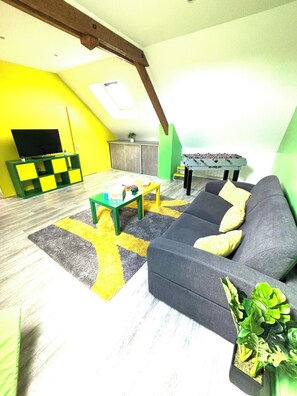 Una sala de estar con sofá, mesa de centro, televisor y mesa de futbolín.