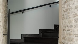 A wooden staircase with a metal handrail, leading to a room with a white wall and a stone-textured accent wall.
