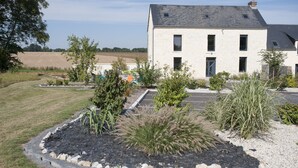 A two-story house with a sloped roof, surrounded by a landscaped garden with various plants and a gravel driveway.