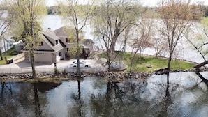 A residential area with a house, a driveway, and a body of water reflecting the surroundings. - Lakefront Family Getaway! Pontoon Rentals-Kayak-Pedal Boat-Fire Pit-Sandy Beach (Lindstrom)