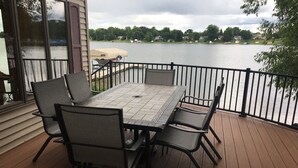 A wooden deck with a table and chairs, overlooking a lake with houses in the background. - Lakefront Family Getaway! Pontoon Rentals-Kayak-Pedal Boat-Fire Pit-Sandy Beach (Lindstrom)