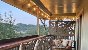 Een houten terras met metalen stoelen en een bank, een decoratief scherm, en uitzicht op het landschap.