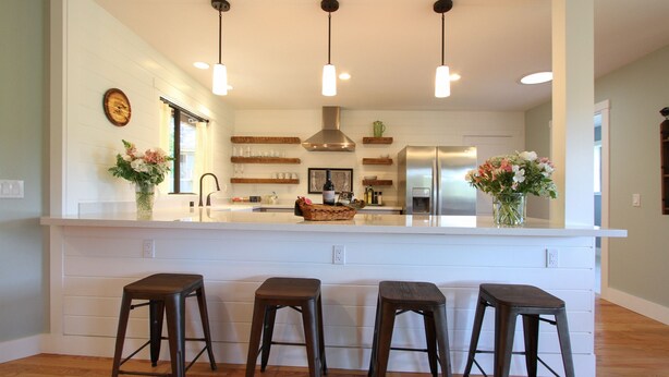 Een moderne keuken met een centraal eiland, barstoelen, hanglampen en houten planken.