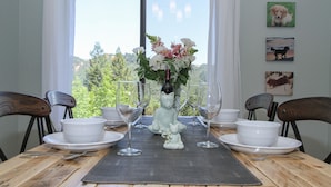 Een eettafel gedekt met witte borden, kommen en wijnglazen, met een bloemenvaas in het midden.