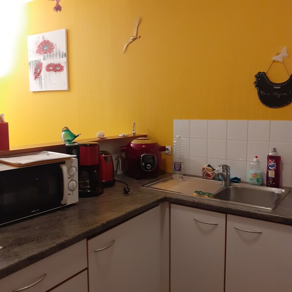 Una cocina con pared amarilla, microondas, cafetera roja, fregadero y una decoración de pájaro.