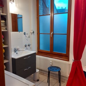 A bathroom with a window, a radiator, a sink, and a mirror. - Apartment with parking in the medieval city, 100 m from the quay, shops. (Saint-Valery-Sur-Somme)