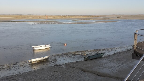 Un paysage côtier avec des bateaux sur la plage, une étendue de sable et un ciel dégagé.