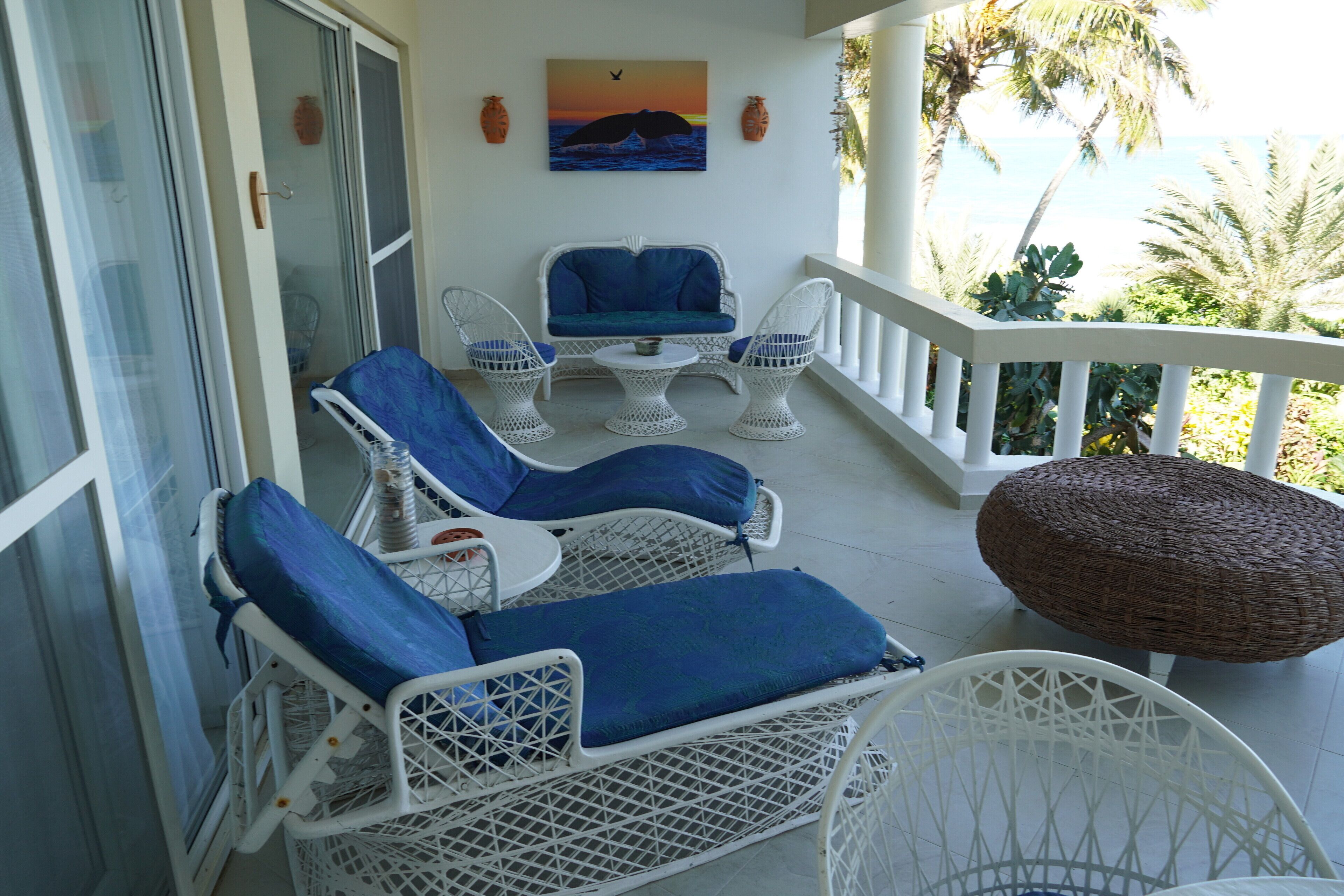 Un balcón con mobiliario de mimbre blanco, incluyendo sillones y una mesa, con vista a una playa.