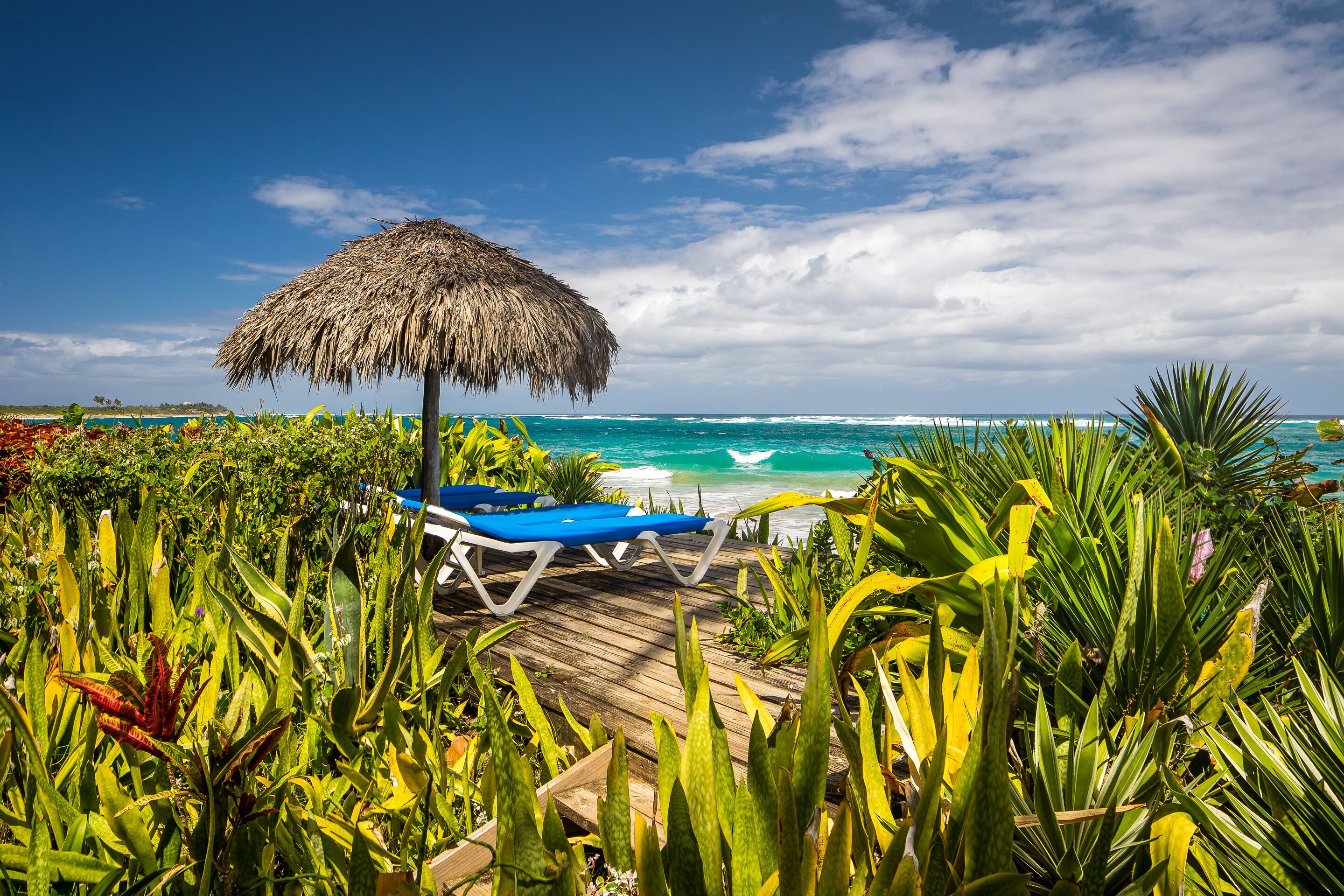 A wooden deck with a thatched umbrella and a blue lounge chair by the ocean.