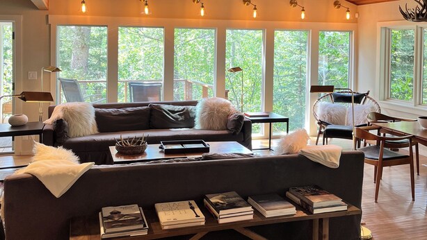 A spacious living room with a large sofa, multiple windows, and a wooden ceiling. - Ski-In Family Lodge w/ Hot Tub, Game Room, Sauna & Designer Interiors (Teton Village)