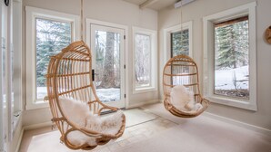 A room with two wicker chairs with white fur throws, large windows with snowy views, and a light-colored floor. - Ski-In Family Lodge w/ Hot Tub, Game Room, Sauna & Designer Interiors (Teton Village)