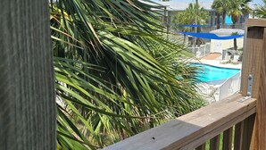 A wooden deck with a view of a swimming pool and palm trees. - Port Aransas condo in the heart of town' LP217B (Port Aranasas)