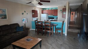 A living room with a brown sofa, a wooden coffee table, and a dining area with wooden chairs and a table. - Port Aransas condo in the heart of town' LP217B (Port Aranasas)
