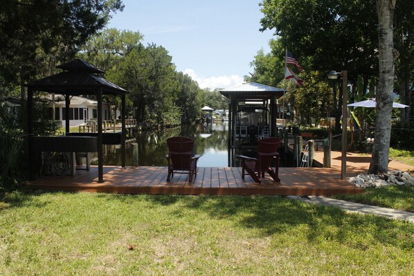A riverside deck with wooden chairs and a gazebo, surrounded by trees and a calm water body. - Homosassa Waterfront with boat dock deep-water canal (Homosassa)