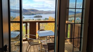 Une terrasse en bois avec une porte vitrée donnant sur un balcon qui offre une vue sur un lac et des collines.