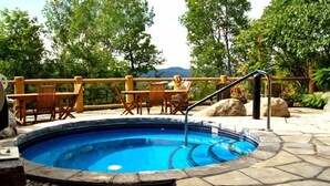 Une piscine circulaire bordée de pierres, entourée de meubles de jardin en bois et d’une rambarde en bois.