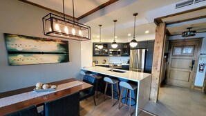 Une cuisine moderne dotée d’un îlot central, de tabourets de bar, de luminaires suspendus et d’un tableau au mur.