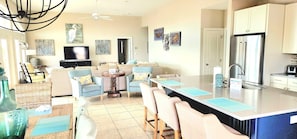 A modern kitchen with a large island, dining area with chairs, and a television in the living room.