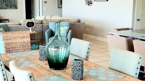 Uma área de refeições com mesa de madeira, cadeiras acolchoadas, um lustre decorativo e um vaso grande.