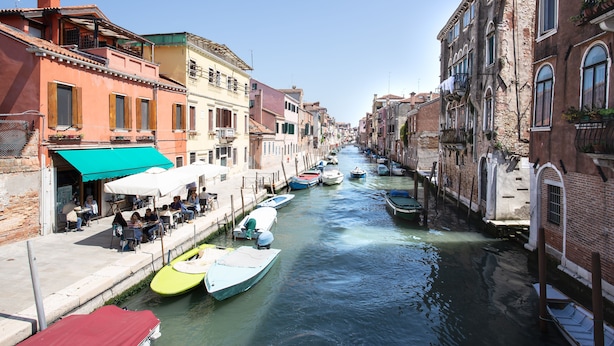 A canal lined with buildings, boats docked along the water, and outdoor seating areas.