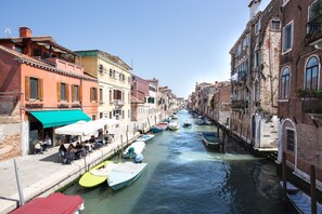 Ein Kanal, gesäumt von Gebäuden, mit am Wasser liegenden Booten und Außenbereichen mit Sitzgelegenheiten.