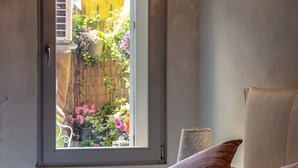 A bedroom with a window, a bed with pink pillows, a wall-mounted light fixture, and a potted plant.