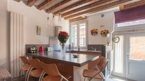 A modern kitchen with a central island, wooden beams, and a view to the outside.