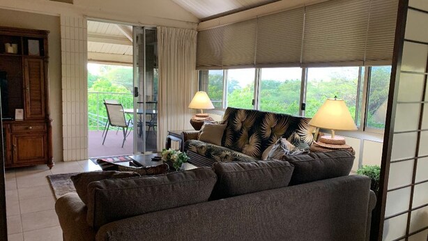A living room with a sofa, two lamps, a table, and a view of greenery outside. - 2 bdrm 2 Bath Condo with Partial Ocean Views, Steps away from Kamaole III Beach  (Kihei)