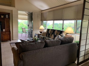 Un salon avec un canapé, deux lampes, une table et une vue sur la verdure à l’extérieur.