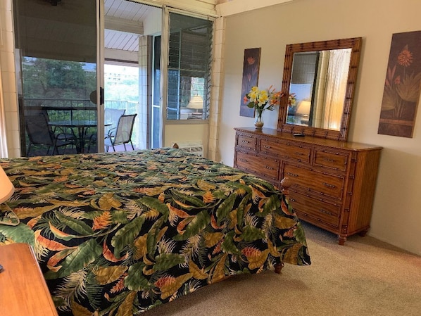 Une chambre à coucher avec un lit, une commode en bois, un miroir et une fenêtre donnant sur l’extérieur.