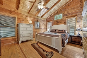 Une chambre dans une cabane en bois, avec un lit, une commode et un ventilateur de plafond.