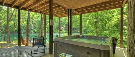 A hot tub under a wooden deck with a view of a forested area.