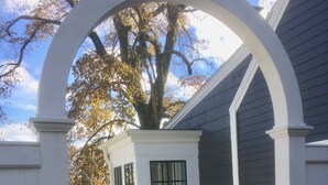 A white wooden structure with a window, surrounded by a stone base and a leaf-covered ground.