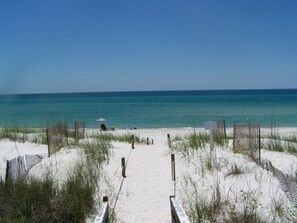 A beach pathway leading to the ocean with a fence on either side and a person sitting under a beach umbrella. - Barefoot Getaway is your perfect poolside paradise!
 (Port Saint Joe)
